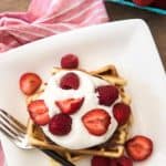 Belgian waffles on a white plate with whipped cream and fresh strawberries and raspberries.