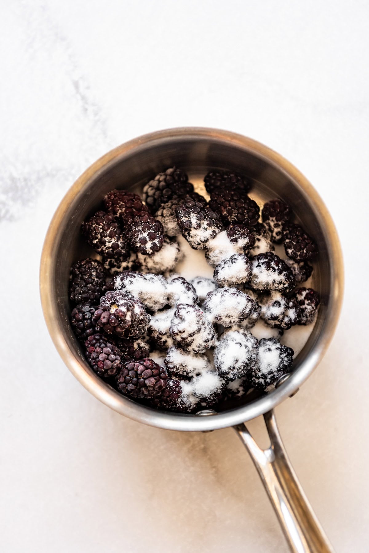 Combining fresh blackberries and sugar in a saucepan.