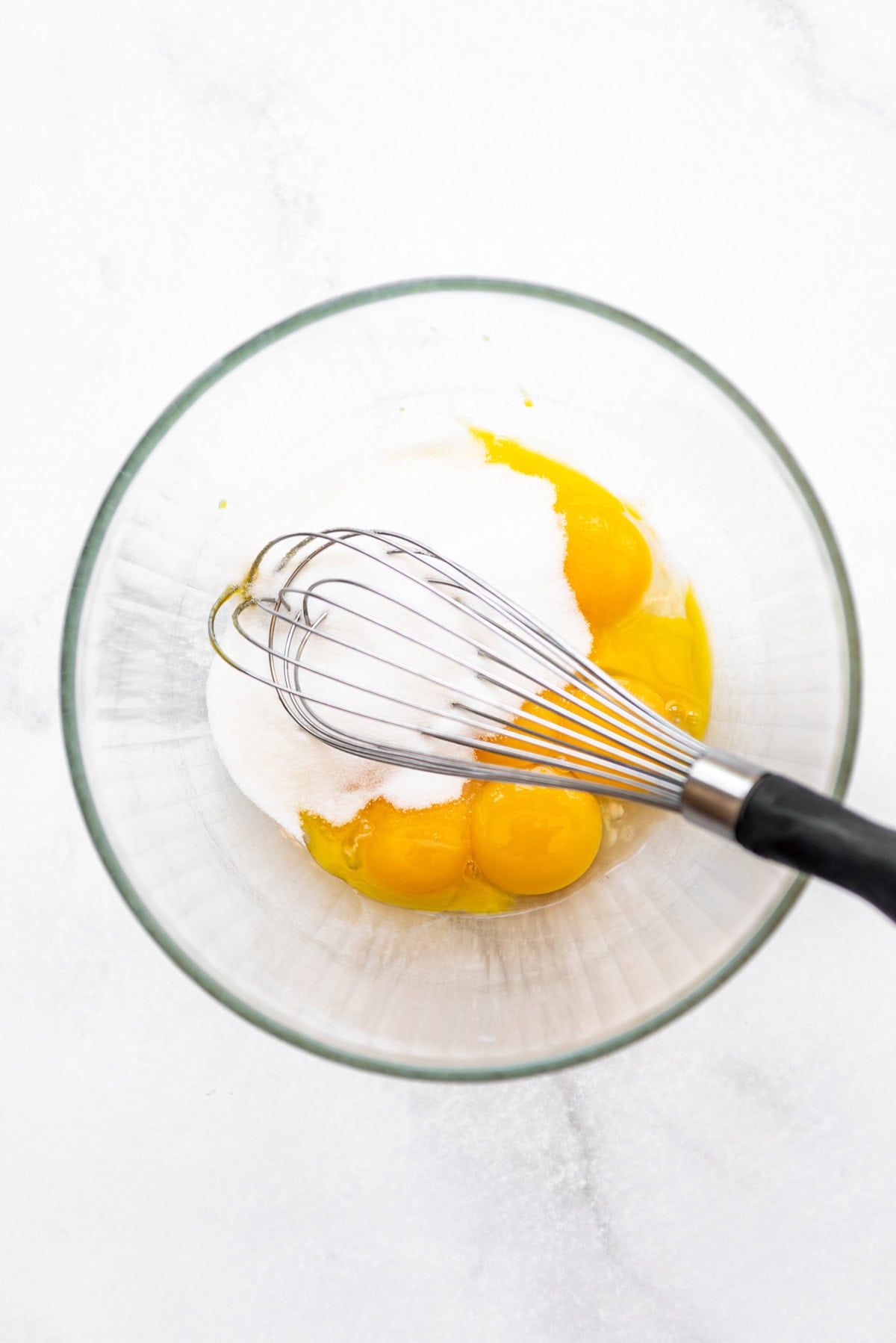 A whisk in a bowl of granulated sugar and egg yolks.