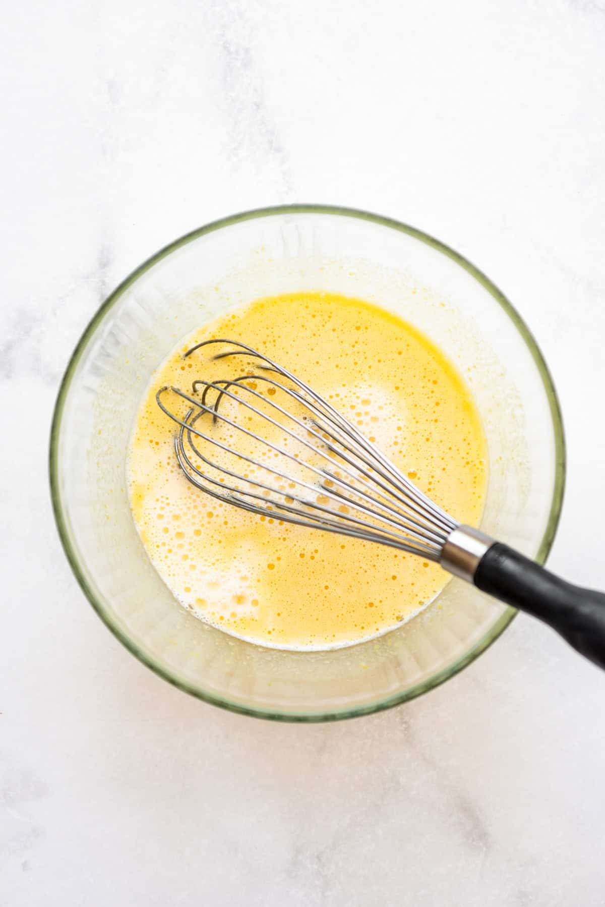 Tempering egg yolks with hot liquid in a bowl with a whisk.