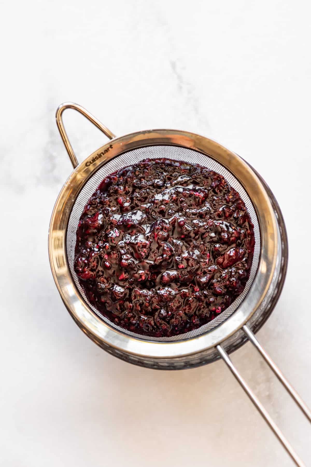 Straining blackberry jam through a fine mesh strainer to remove seeds.