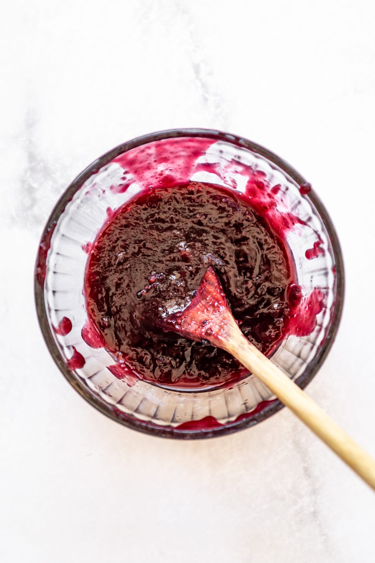 Blackberry puree in a glass bowl with a wooden spoon.