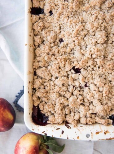 A blackberry nectarine crumble in a baking dish next to fresh nectarines.