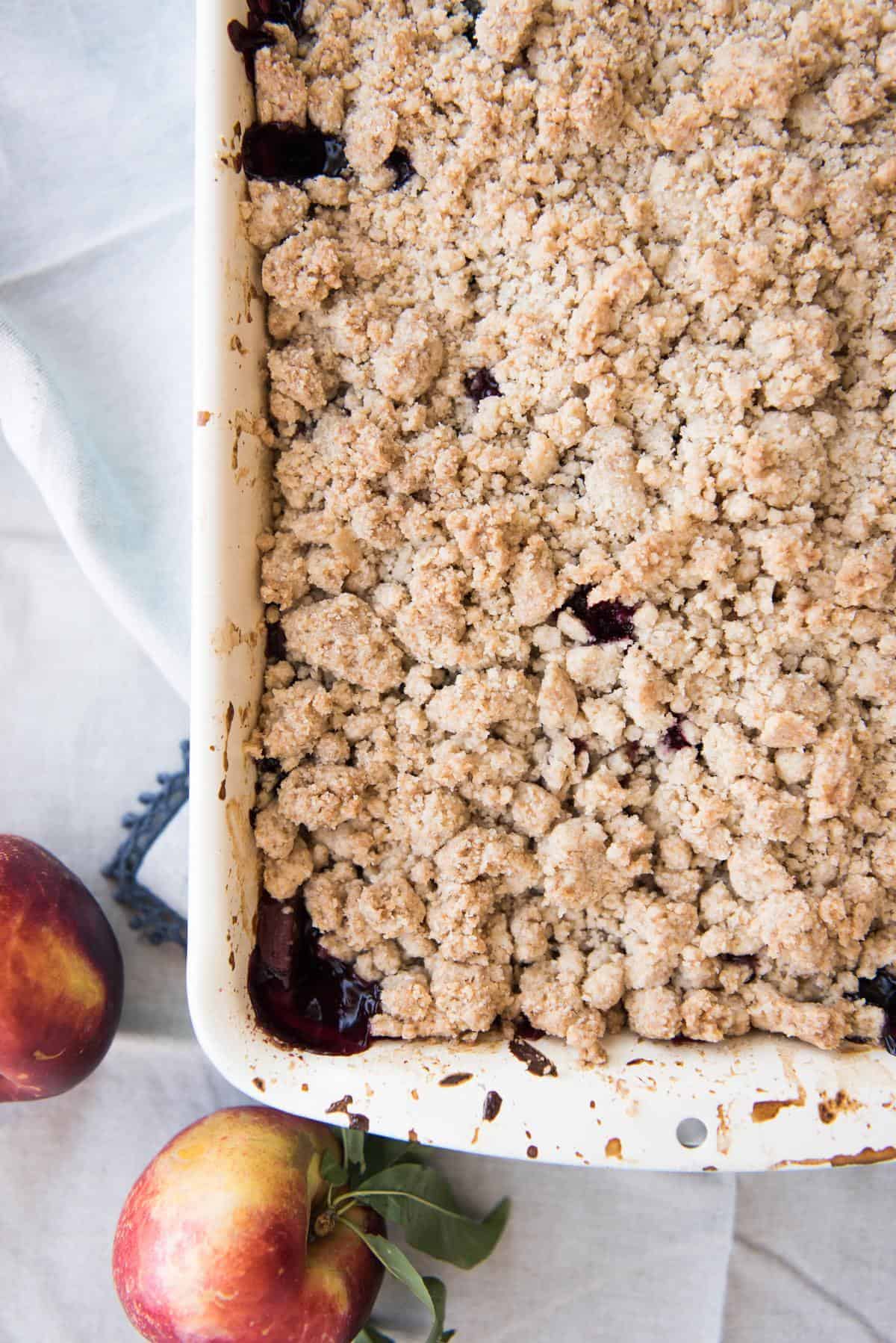 A blackberry nectarine crumble in a baking dish next to fresh nectarines.