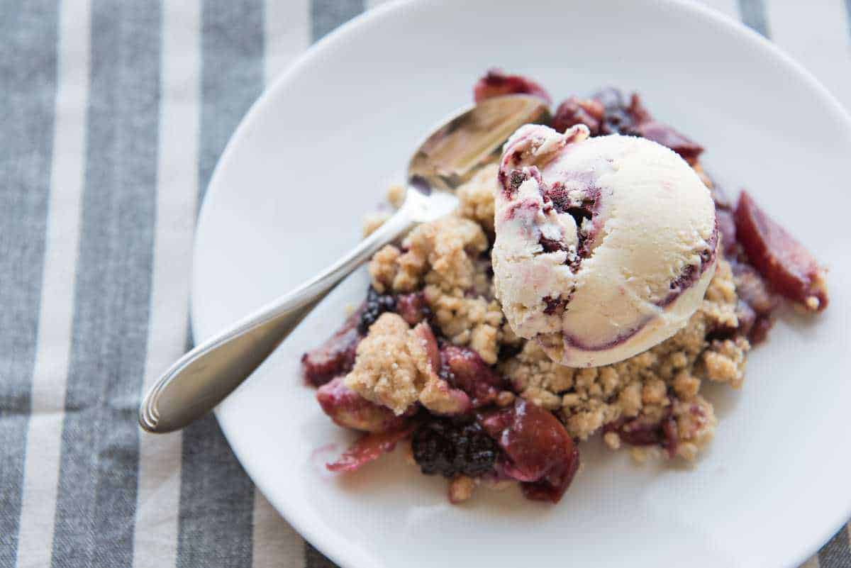 An image of a plate of blackberry nectarine crumble served with ice cream.