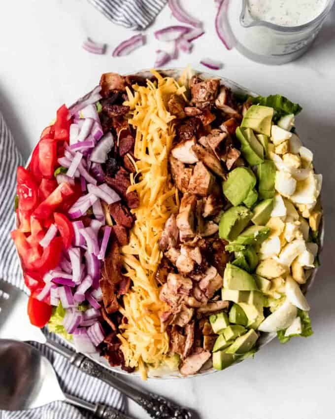 An overhead image of a bbq chicken cobb salad with the ingredients arranged in rows on top of a bed of romaine lettuce.