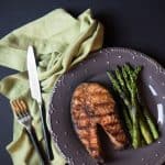 A grilled salmon steak on a plate with grilled asparagus.