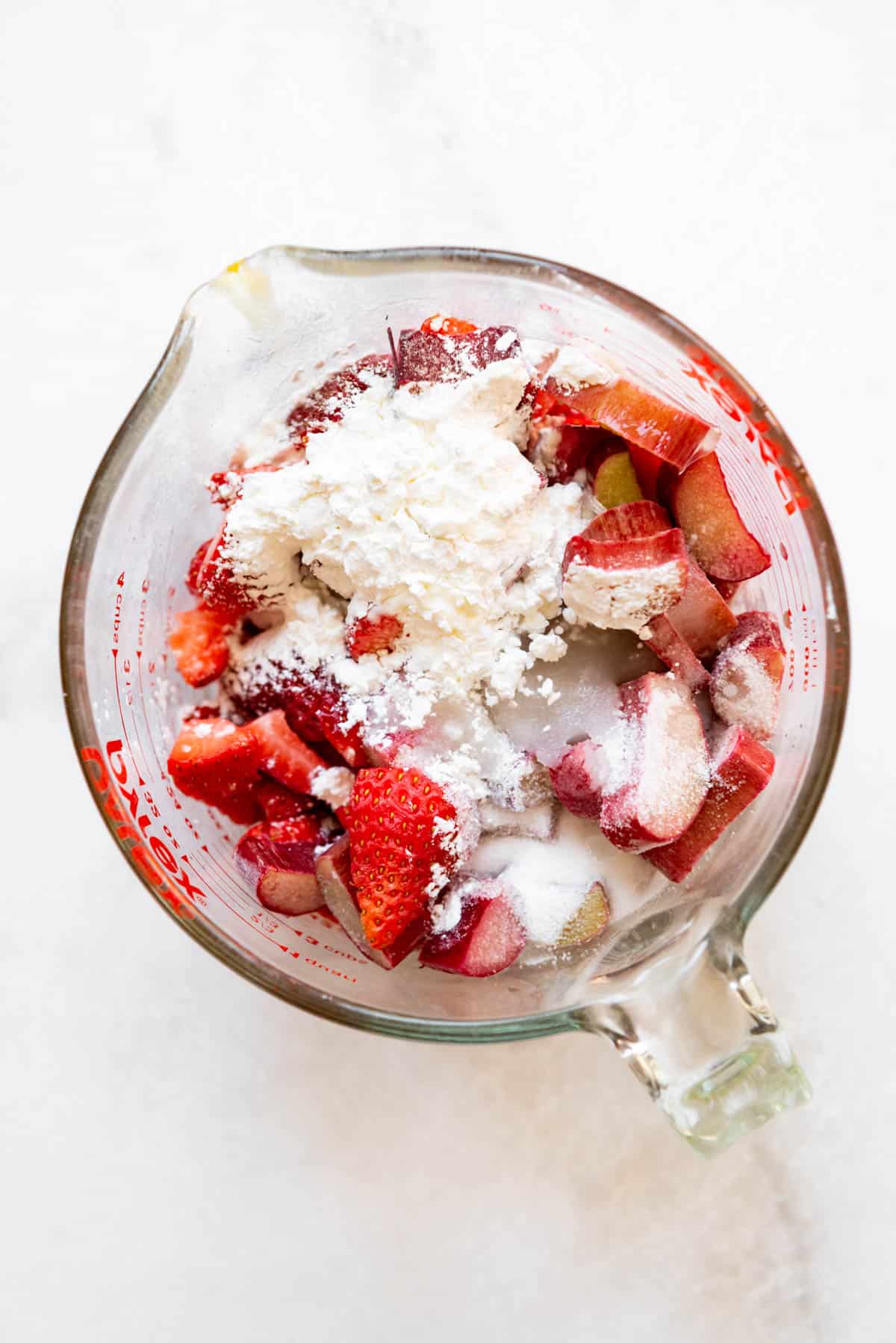 Combining strawberries, rhubarb, cornstarch, sugar, and lemon juice in a glass bowl to make a filling.