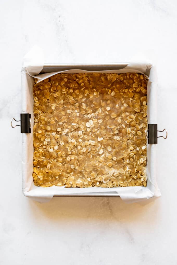 Pressing oat mixture into a square baking dish lined with a parchment paper sling.