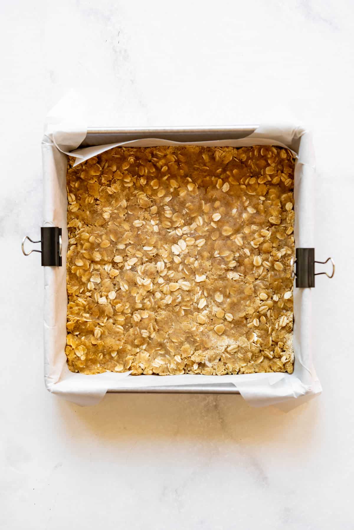 Pressing oat mixture into a square baking dish lined with a parchment paper sling.