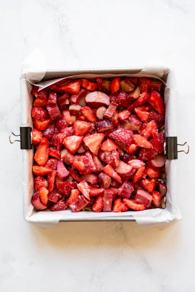 Adding a layer of strawberry rhubarb filling to a square baking dish.