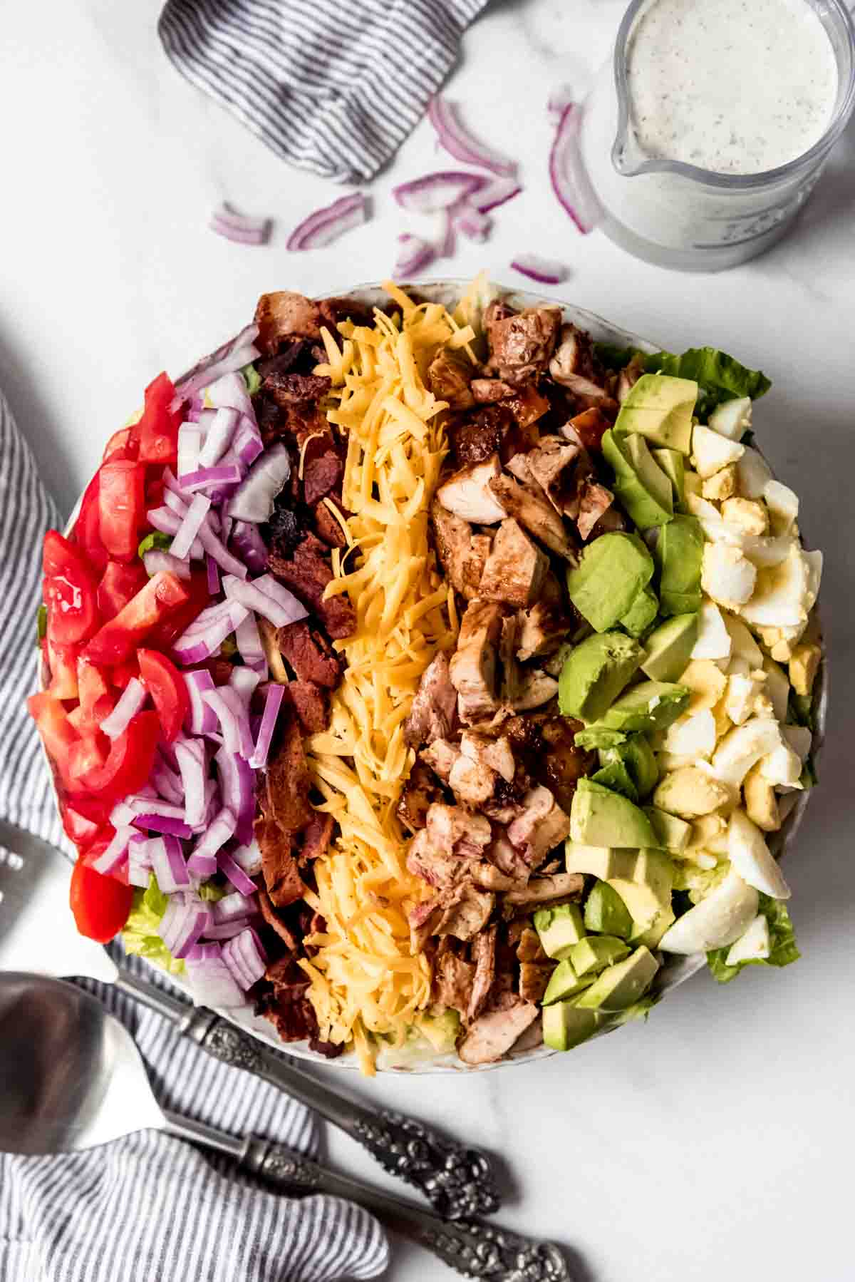 An overhead image of a bbq chicken cobb salad with the ingredients arranged in rows on top of a bed of romaine lettuce.