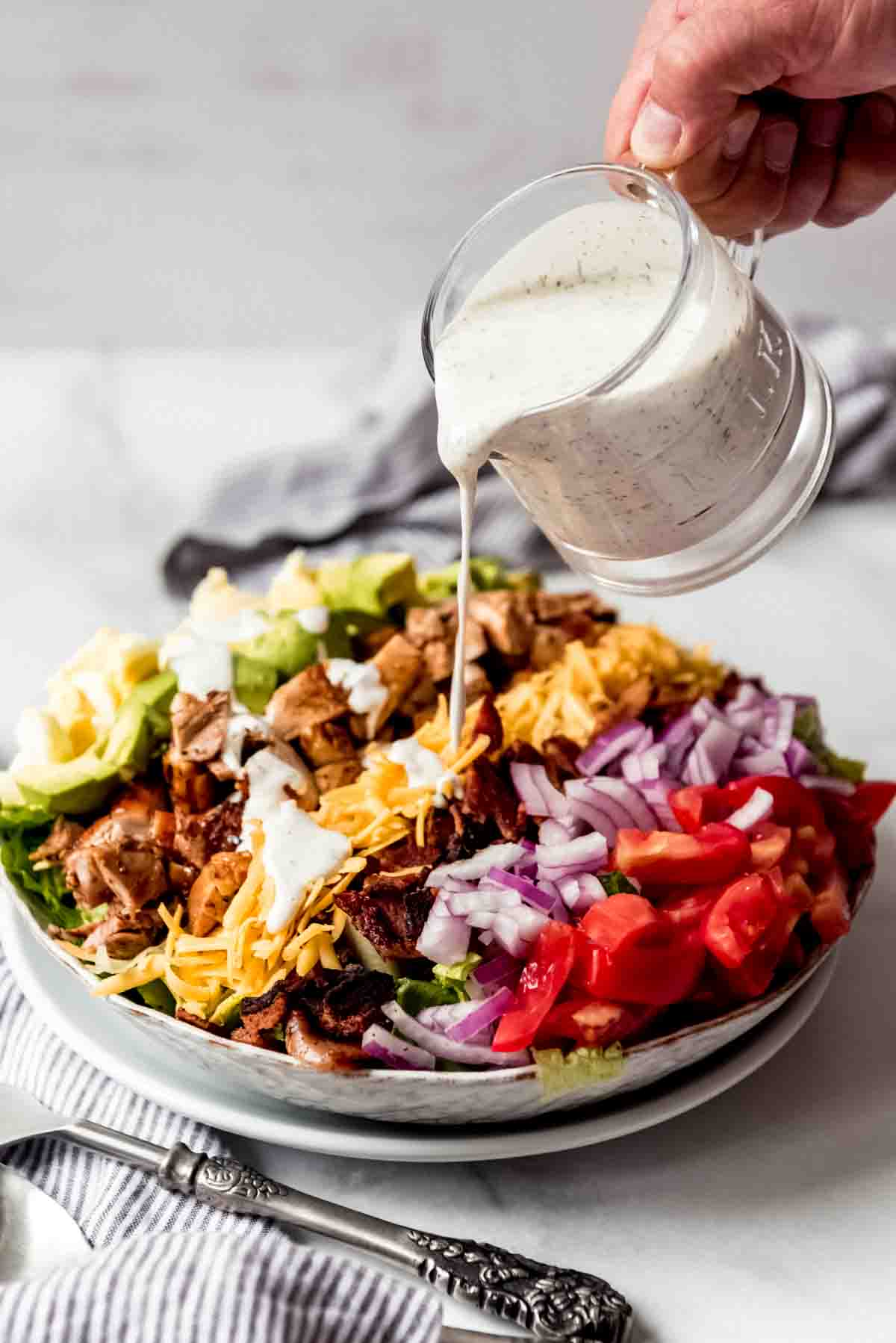 Ranch dressing being poured over a chicken cobb salad.