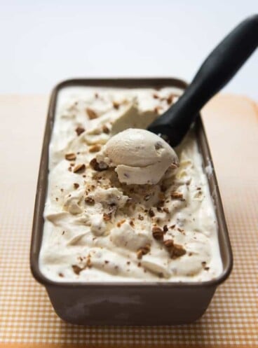 A container of homemade toasted almond ice cream with a scoop being scooped out.