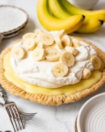 A homemade banana cream pie in front of a bunch of ripe bananas.