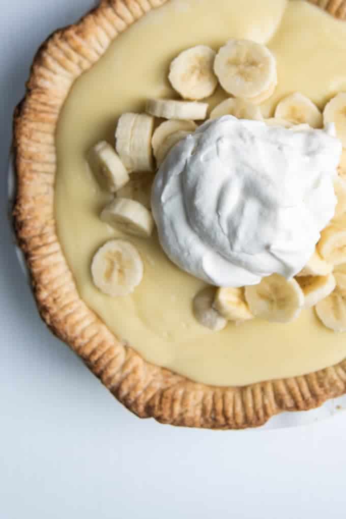 A homemade banana cream pie topped with fresh, sliced bananas and whipped cream.