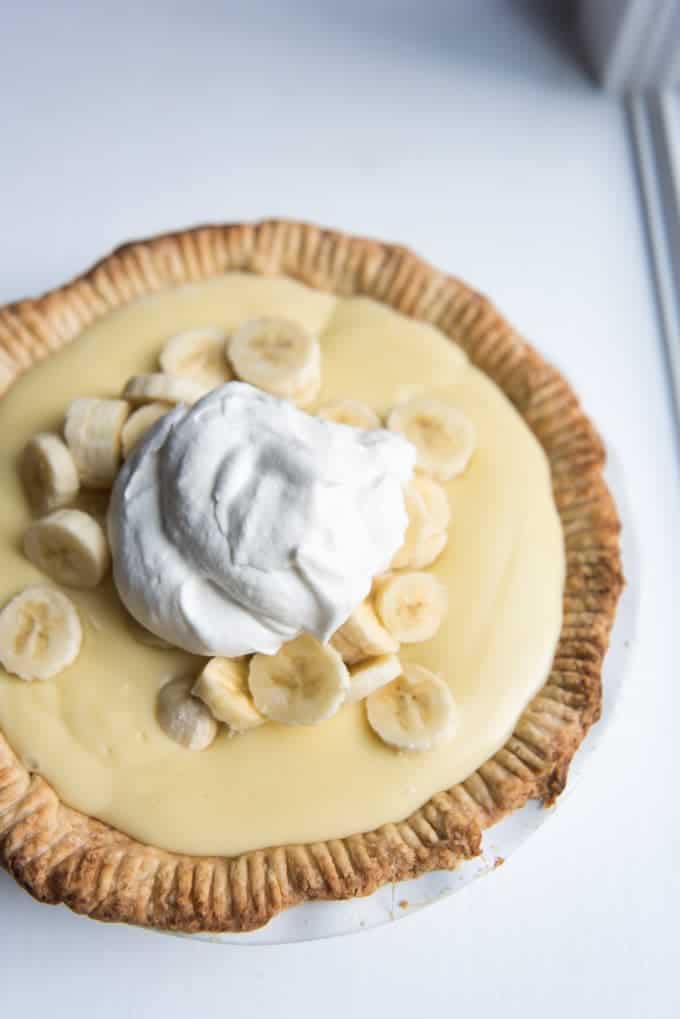 An old-fashioned banana cream pie in a homemade crust topped with sliced bananas and a pile of freshly whipped cream.