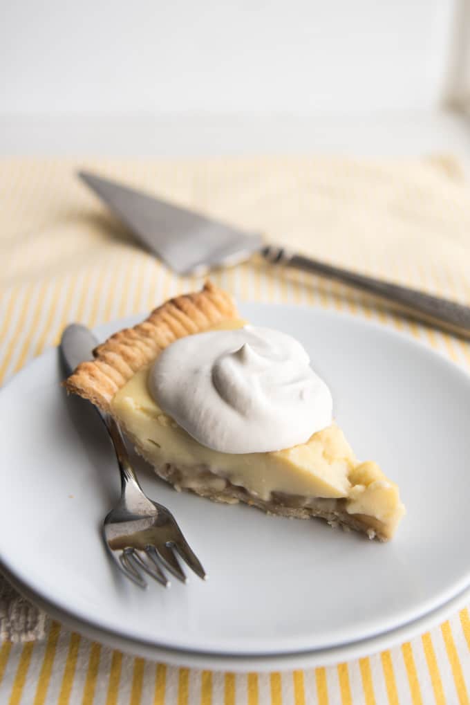A slice of fresh banana cream pie topped with sweetened whipped cream on a plate with a fork.