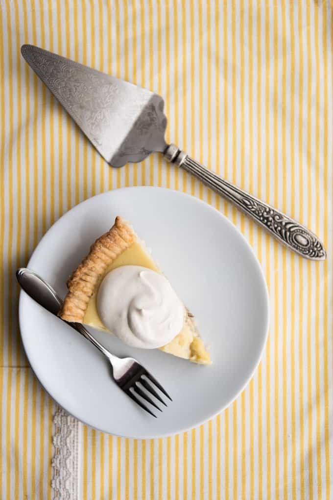 A slice of banana cream pie on a white plate with whipped cream, next to a pie server.