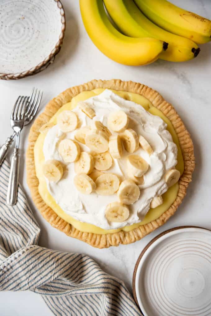 An old-fashioned banana cream pie next to bananas and a striped linen napkin.