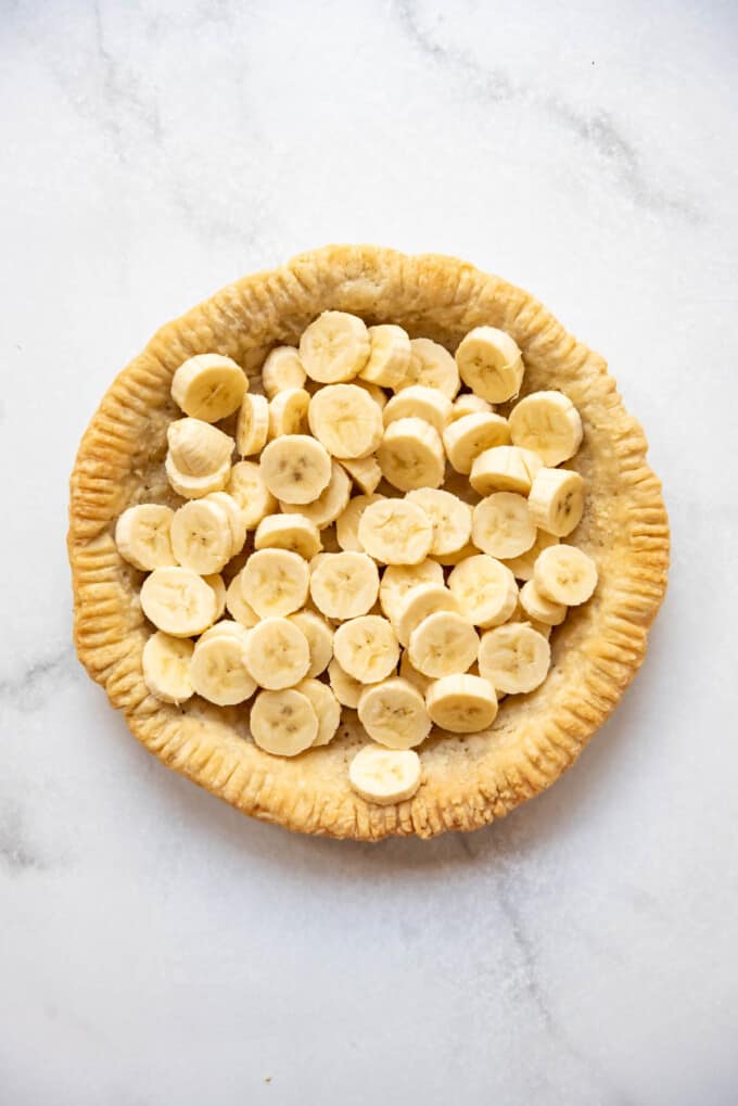 A layer of sliced fresh bananas in a homemade pie crust that has been blind-baked.
