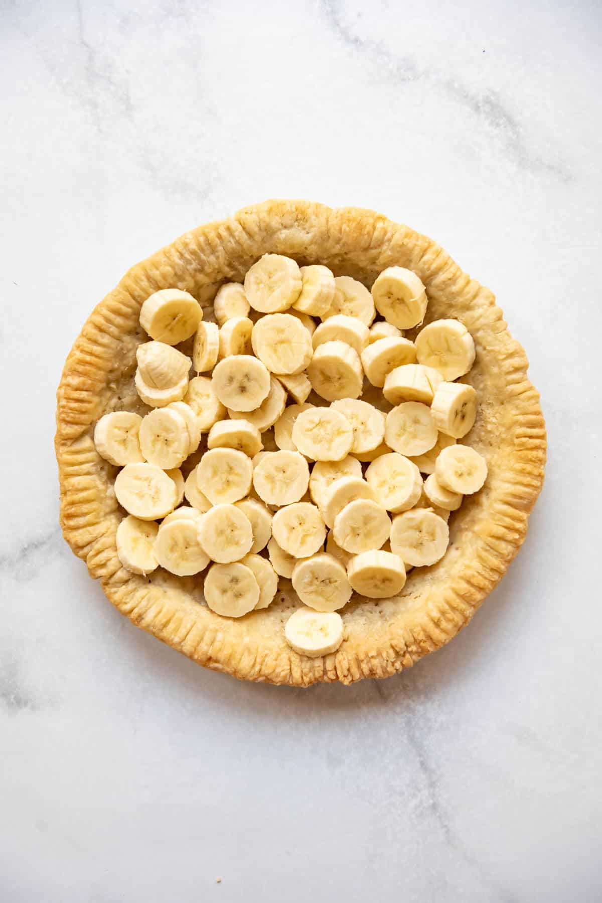 A layer of sliced fresh bananas in a homemade pie crust that has been blind-baked.