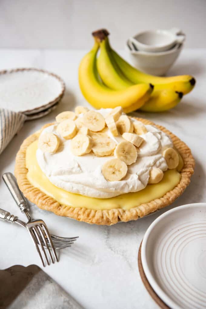 A homemade banana cream pie in front of a bunch of ripe bananas.