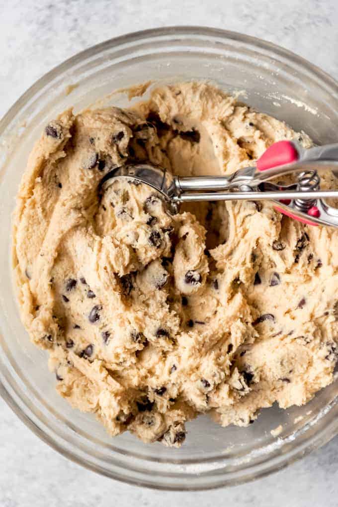 An image of a bowl of chocolate chip cookie dough with a cookie scoop in it.