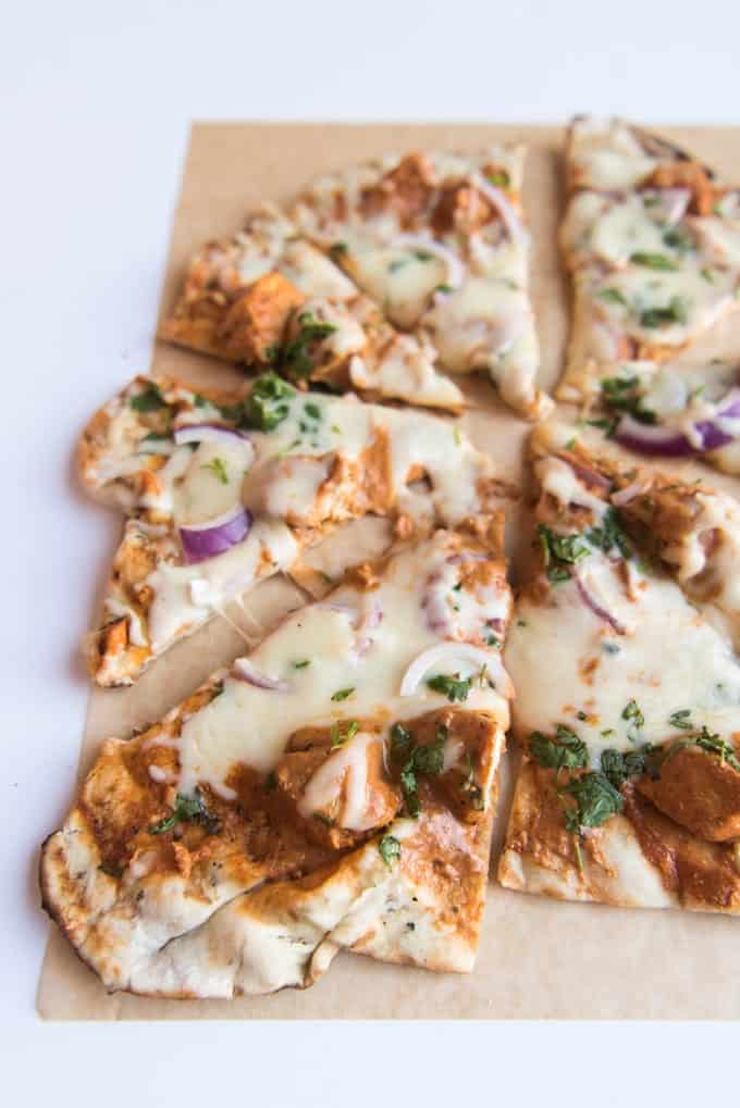 a close up view of sliced chicken tikka masal pizza slices on parchment paper