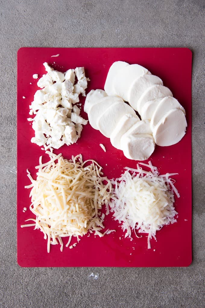 An image of fresh mozzarella, fontina cheese, goat cheese, and pecorino romano on a red cutting board.