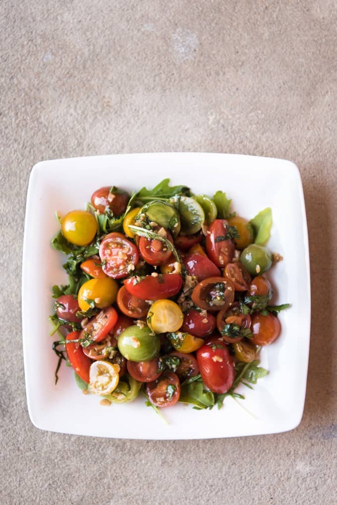 A white plate with tomato, basil, and arugula salad.