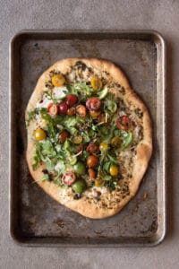 A four cheese pizza with a tomato, basil, and arugula salad on top.