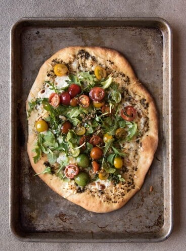 A four cheese pizza with a tomato, basil, and arugula salad on top.