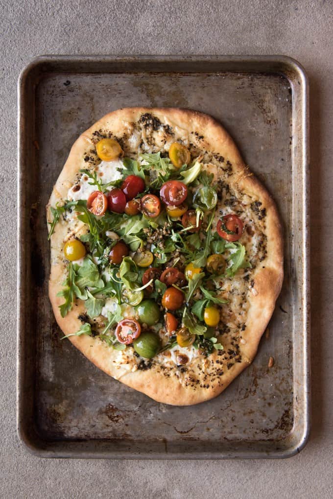 A homemade cheese pizza topped with a tomato basil arugula salad.