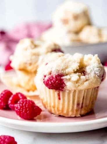 a close up view of raspberry streusel muffin on a plate with fresh raspberries
