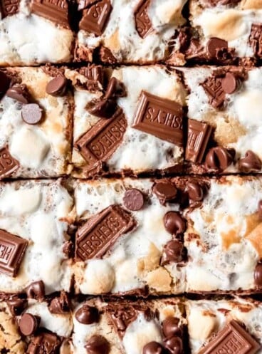 A close-up image of s'mores chocolate chip cookie bars topped with marshmallows and Hershey's chocolate.