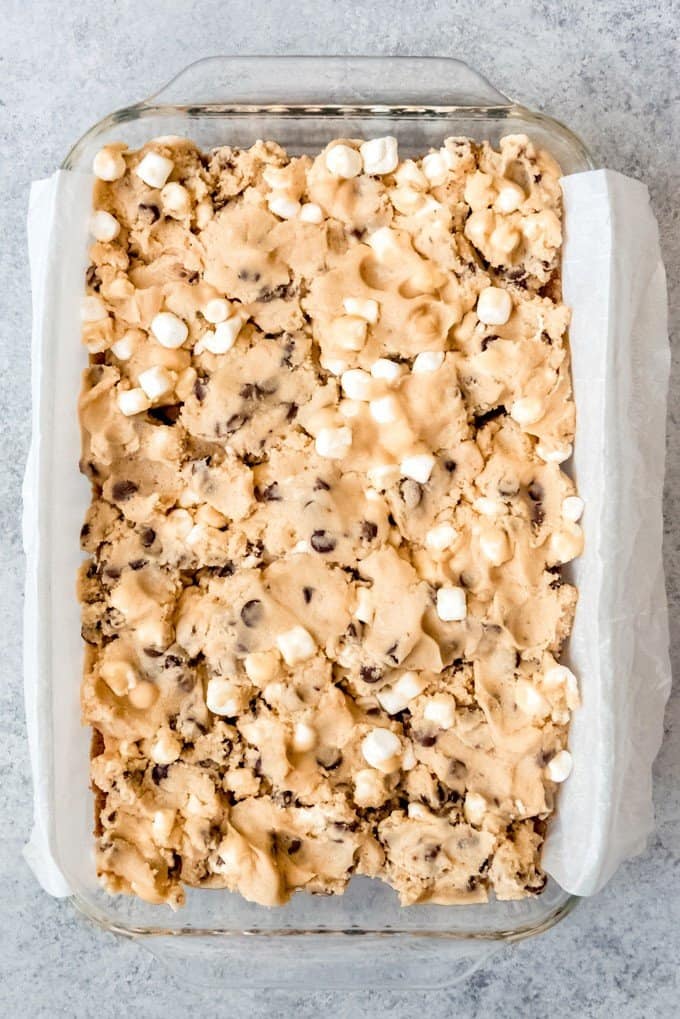 An image of chocolate chip cookie dough pressed into a 9x13-inch baking dish on a graham cracker crust.