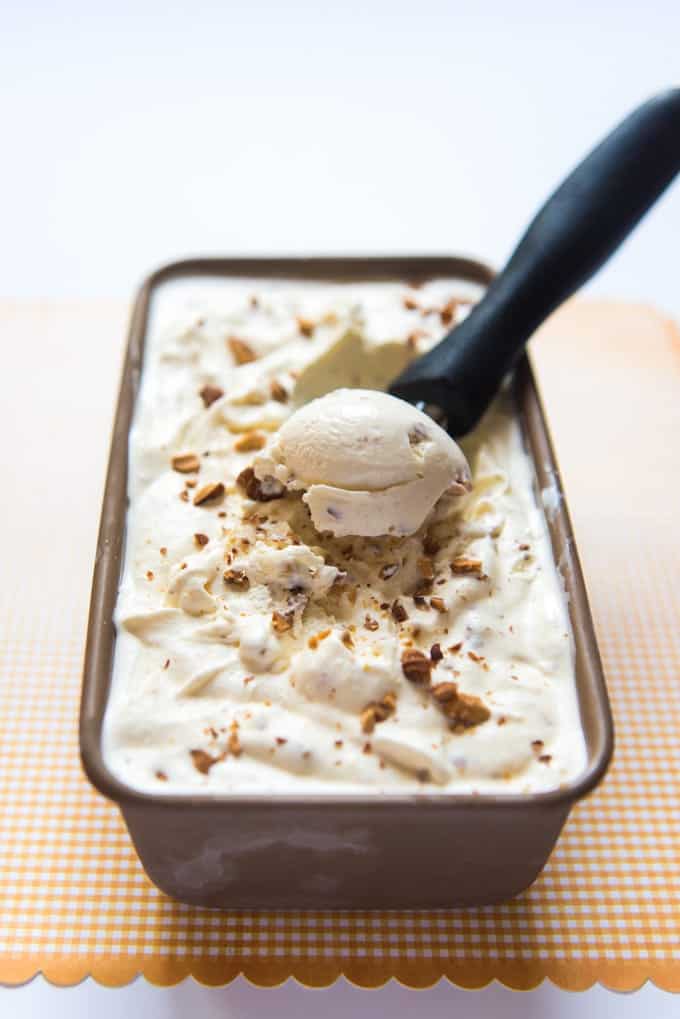 Toasted almond ice cream being scooped out of a pan with an ice cream scoop.