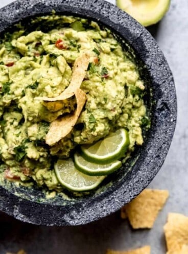 A bowl full of guacamole topped with tortilla chips and lime slices
