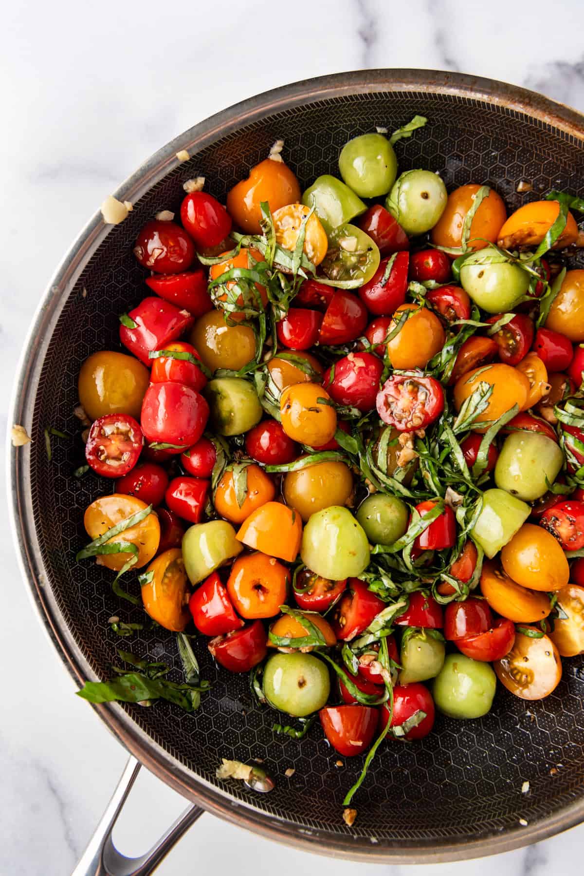 A close up image of grape tomatoes in a pan with thinly sliced basil.