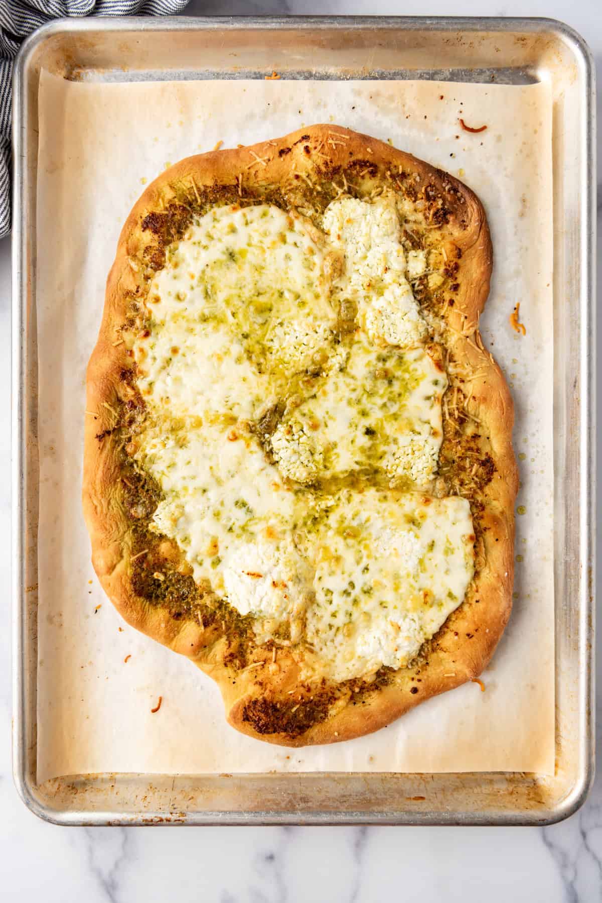 Melted cheeses on top of a pizza made with pesto sauce and a homemade pizza dough.