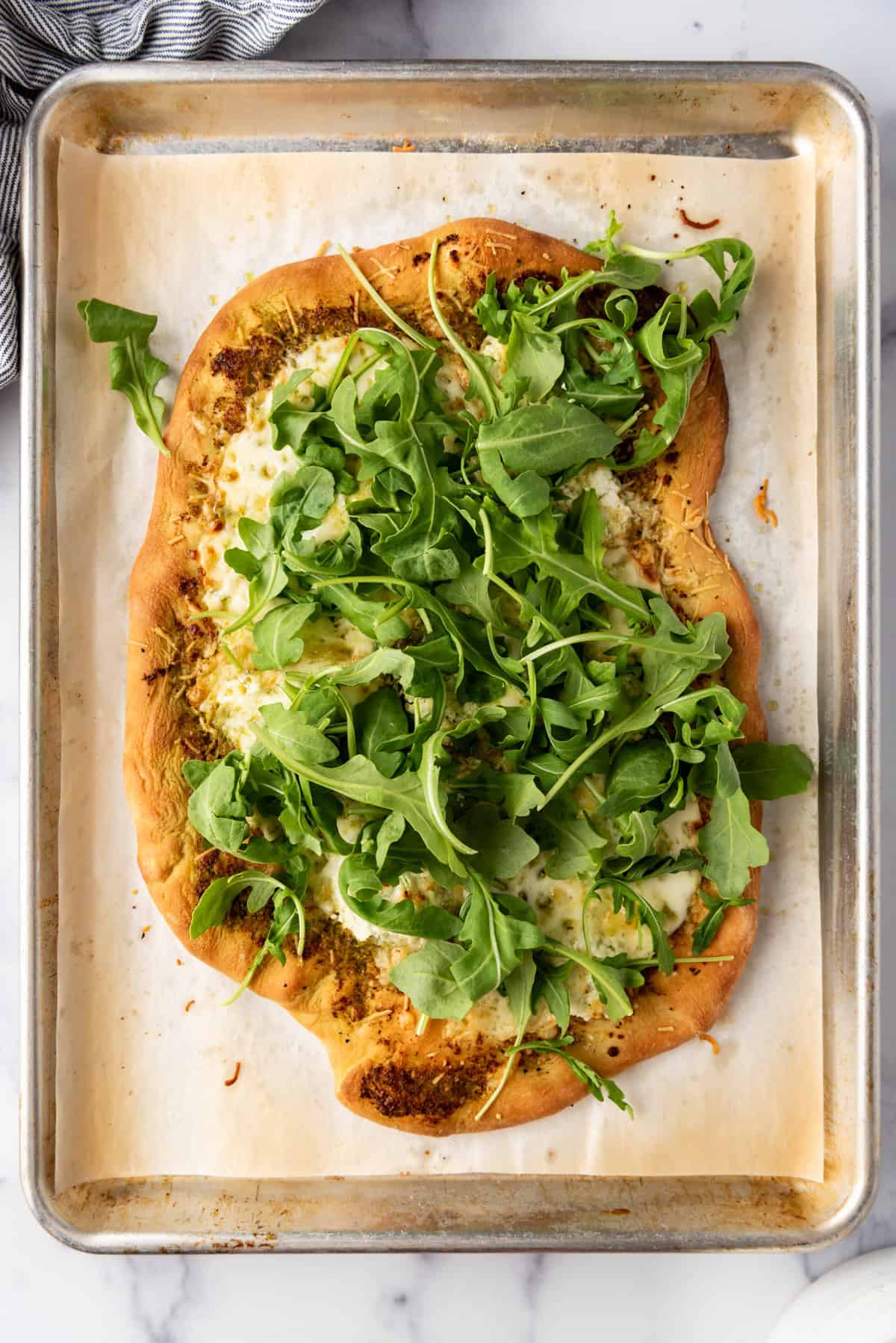 Adding arugula on top of a four cheese pizza.