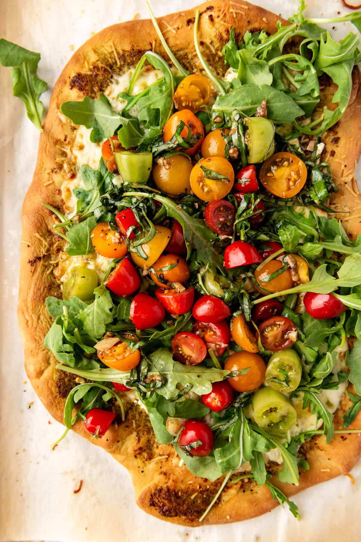 A close overhead image of a four cheese pizza with arugula and fresh tomatoes on top.