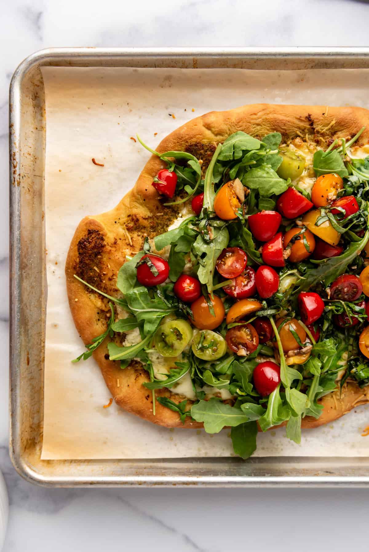 An overhead image of a homemade pizza with tomatoes and arugula.