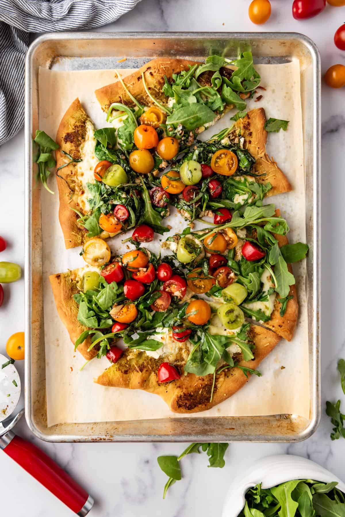 A four cheese pizza topped with tomatoes, basil, and arugula with slices pulled away.