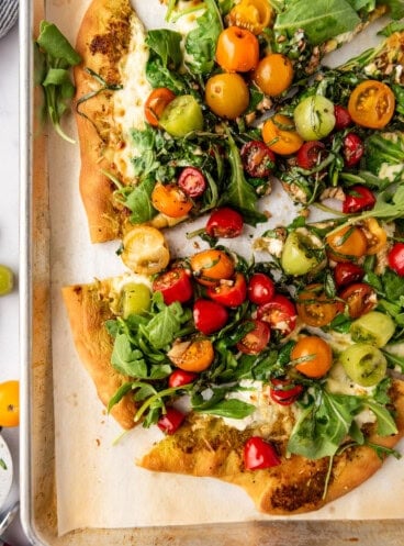 A close overhead image of sliced four cheese pizza with tomato and arugula salad on top.