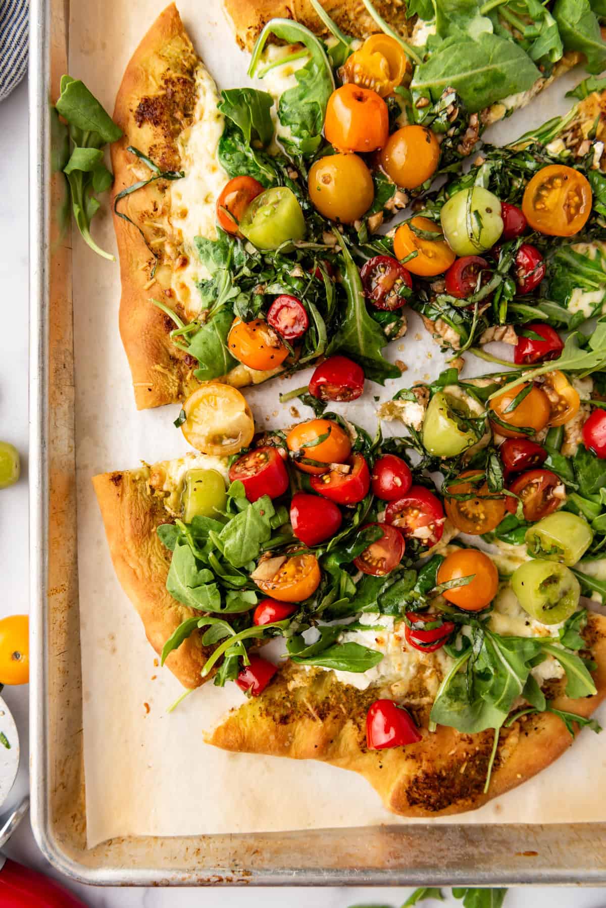 A close overhead image of sliced four cheese pizza with tomato and arugula salad on top.