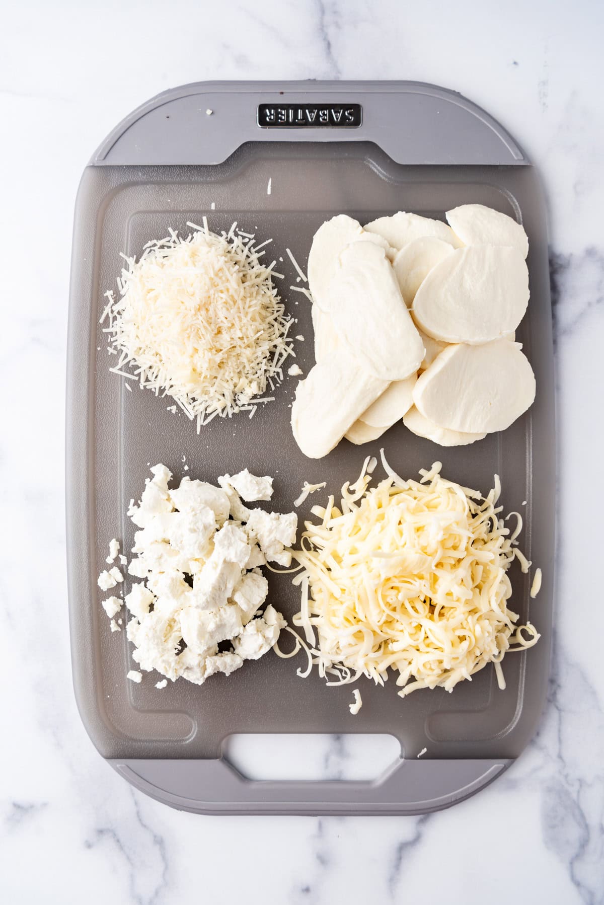 An image of fresh mozzarella, fontina cheese, goat cheese, and pecorino romano on a red cutting board.