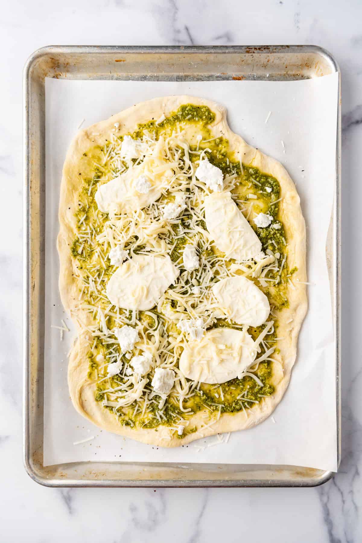 Adding pesto and cheeses to pizza dough.