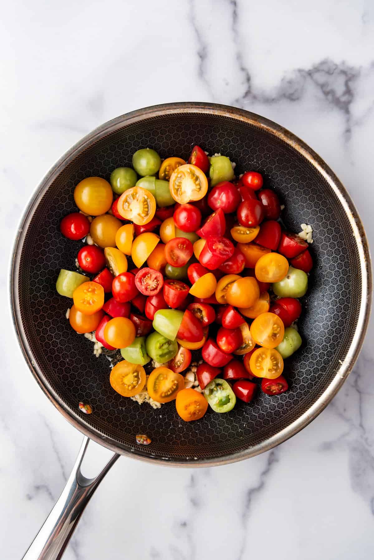 Adding sliced cherry tomatoes to a pan of oil and minced garlic.